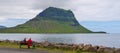 Man and women sitting as the bench in the border of Hvamms Fjord facing to the famous Kirkjufell mountain
